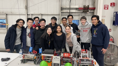 Twelve college students in a lab posing behind several robots on a table.