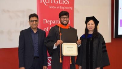 Arpan Gupta holds his diploma while standing between two professors