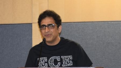 Male with black curly hair with eyeglasses standing behind a podium wearing an ECE black t shirt.