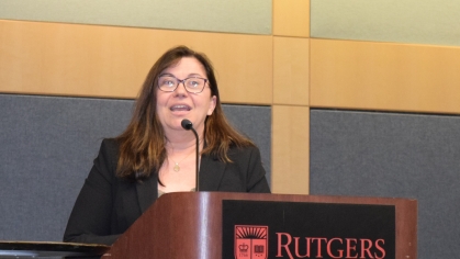 Woman with long brown hair and eyeglasses standing behind a Rutgers podium.