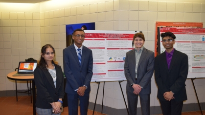 One female and three male students flank their research poster.