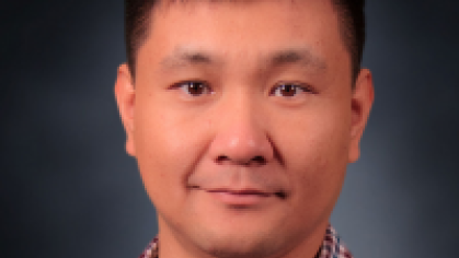 Headshot of man wearing an open collar plaid shirt. He has short black hair.