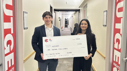 A male and a female student wearing dark suits hold an oversized check.
