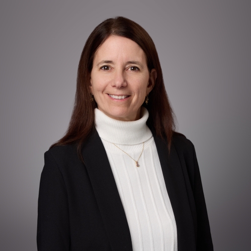 Headshot of female with long brown hair wearing a white turtleneck sweater, a gold necklace, and a black suit jacket.