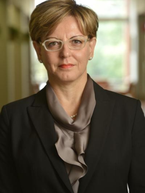 Head shot of woman with short light brown hair, wearing eyeglasses and a dark brown suit and blouse