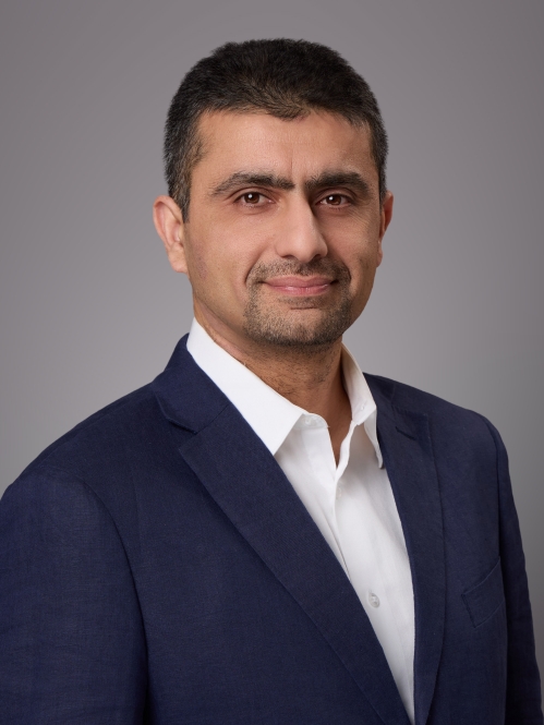 Headshot of male with short black hair, moustache and beard wearing a white button down shirt and a black suit jacket.