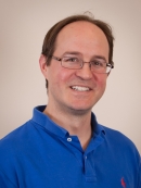 Head shot of balding male with eyeglasses and wearing a blue polo shirt.