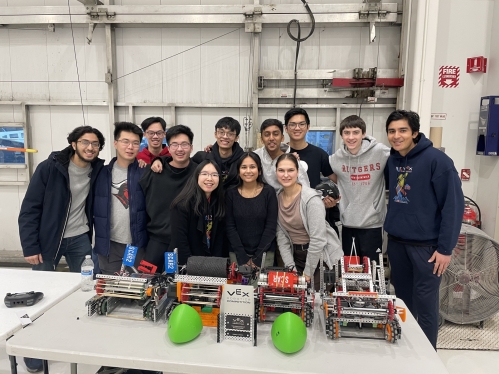 Twelve college students in a lab posing behind several robots on a table.