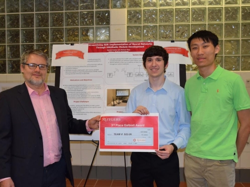 Professor on the left presents an award to two male students on ride. Their research poster is behind all three.