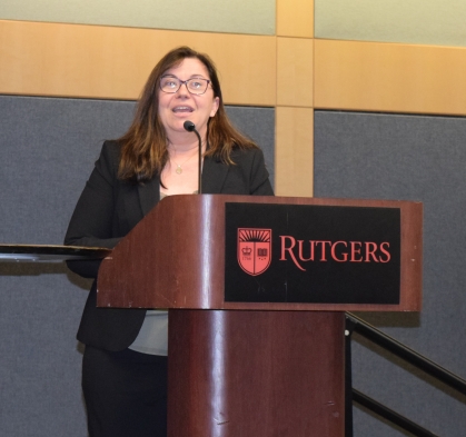 Woman with long brown hair and eyeglasses standing behind a Rutgers podium.