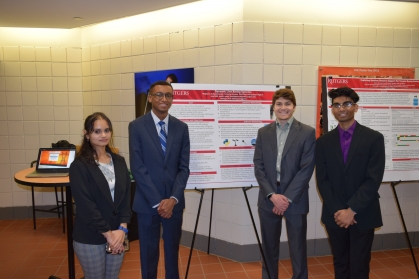 One female and three male students flank their research poster.