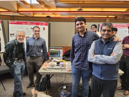 Two male students presenting a senior design project to a male professor and male judge 