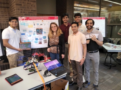 Five male students with a female professor stand behind their senior design.