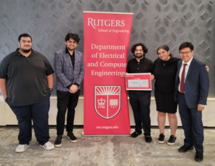 Four male students with a female student flank a red Rutgers Department of Electrical and Computer Engineering banner.