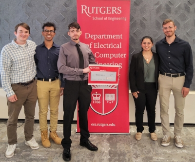 Four male and one female student stand next to a red Rutgers Department of Electrical and Computer Engineering banner.