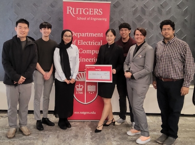 A male professor with three female and three male students flanking a red Rutgers Department of Electrical and Computer Engineering banner.