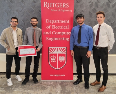 Four male students flank a red Rutgers Department of Electrical and Computer Engineering banner.