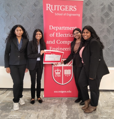 Four female students hold certificate as they stand in front of a red Rutgers Department of Electrical and Computer Engineering banner.