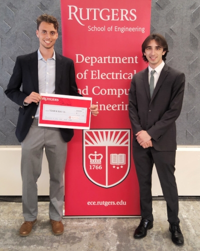 Two male students stand in front of a red Rutgers Department of Electrical and Computer Engineering banner.