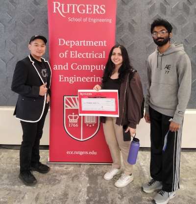 Two male students and one female student holding a certificate stand next to a red Rutgers Department of Electrical and Computer Engineering banner.
