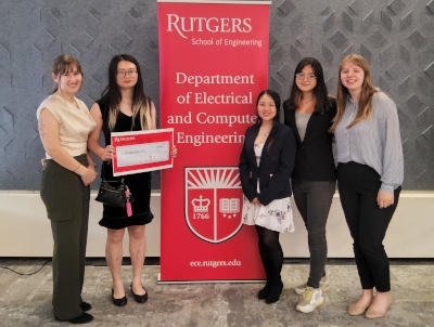 Five female students flank a red rutgers Department of Electrical and Computer Engineering banner.