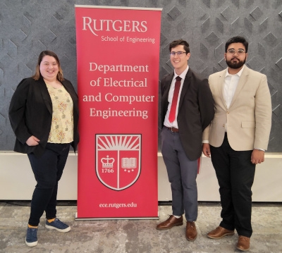 A female and two male students stand next to a red Rutgers Department of Electrical and Computer Engineering banner. 
