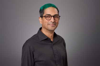 Headshot of male with eyeglasses and green hair wearing a black button down shirt
