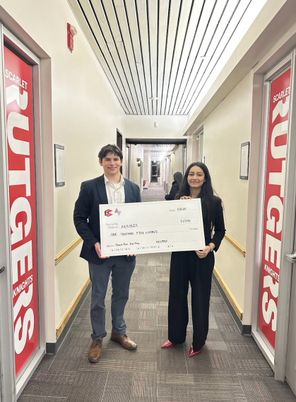A male and a female student wearing dark suits hold an oversized check.