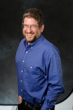 Head shot of male with glasses and beard wearing a blue button down shirt.