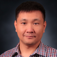 Headshot of man wearing an open collar plaid shirt. He has short black hair.